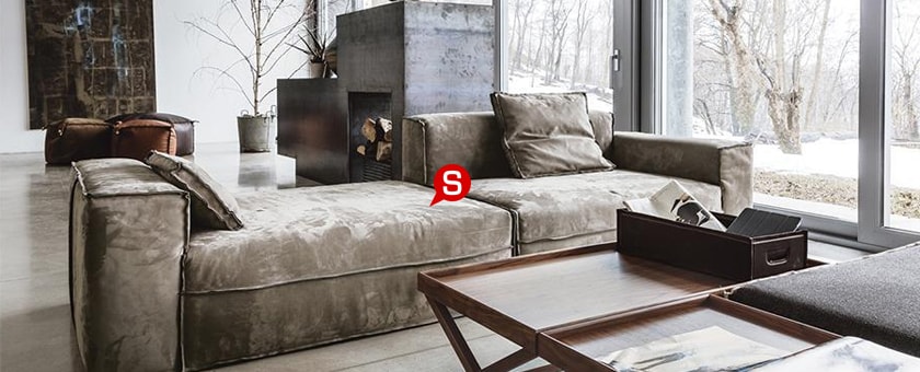 Ein geräumiges Wohnzimmer im Landhausstil mit weißen Wänden und einem großen bequemen Sofa. Im Hintergrund sind bunte Poufs und ein Kamin aus Beton zu sehen.